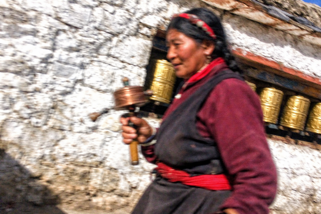 扎什倫布寺轉經道，藏族婦女手持轉經筒繞寺而行，白牆與金色經筒在午後陽光下交錯，日喀則格魯派寺院日常朝聖景象。
