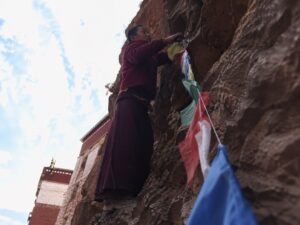 扎耶巴寺崖壁上的藏族男孩正在綁掛經幡，陡峭峭壁與彩色風馬旗，西藏隱修聖地朝聖體驗。
