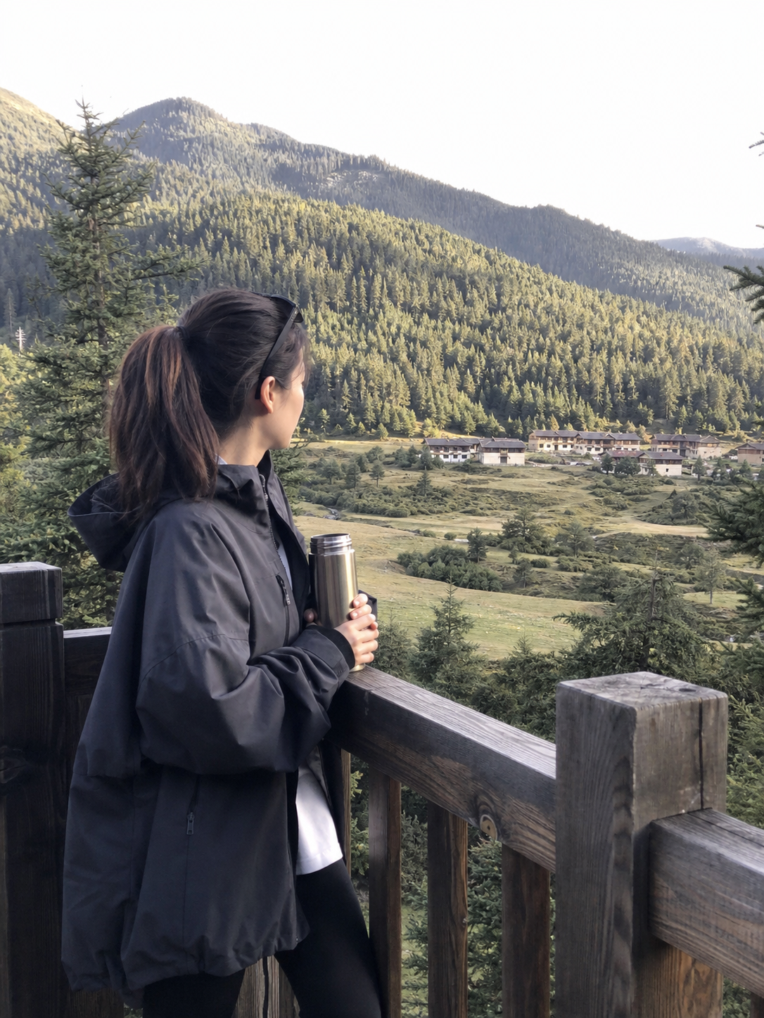 魯朗林海觀景台上旅人拿著保溫杯眺望森林、草甸與藏式村落,林芝魯朗一日遊景點